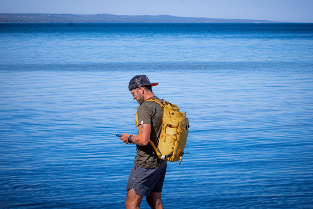 Patrik Widell står vid havet med ryggsäck och mobil i handen.