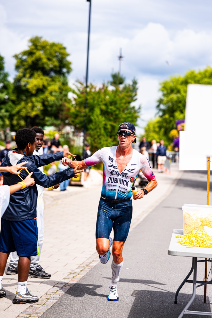 Triathlet tar energi från publik vid vätskestation.